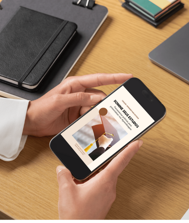 Pessoa segurando um smartphone exibindo a capa do e-book “Domine seus Estudos: Ferramentas práticas para potencializar sua aprendizagem” em um ambiente de trabalho com caderno e laptop ao fundo.